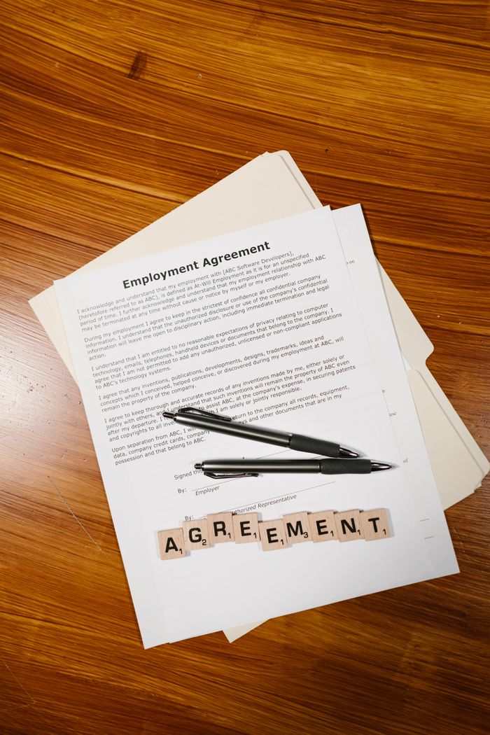 about-us-02 Employment agreement with Scrabble tiles spelling 'AGREEMENT' on wooden surface, captured in detail.