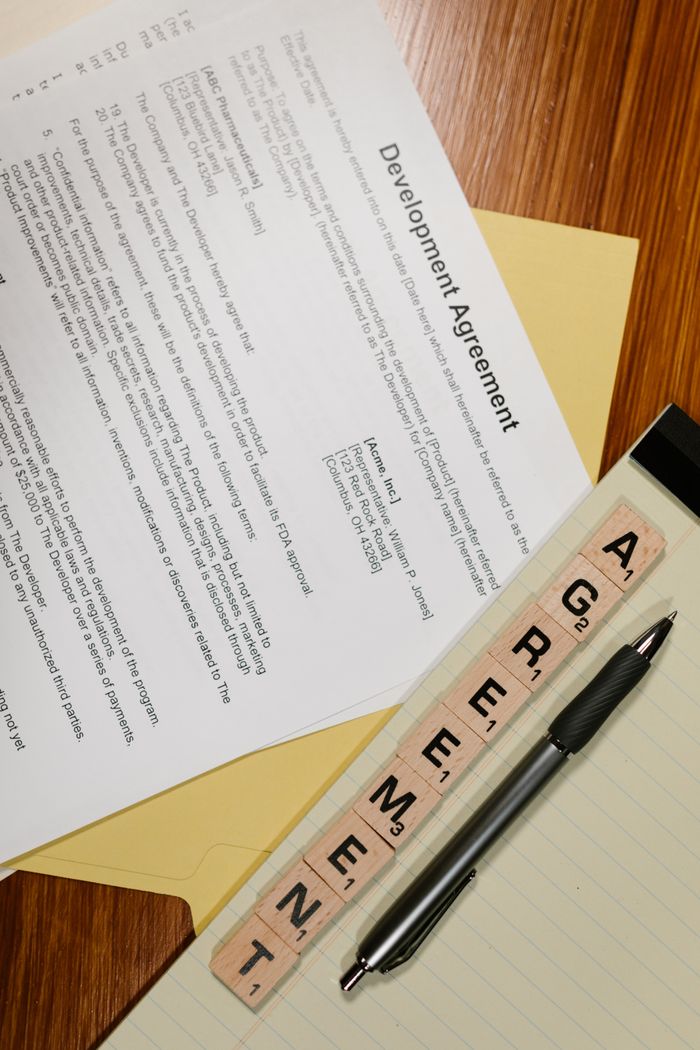 A vertical shot showcasing agreement documents, Scrabble tiles, and a pen on a desk.